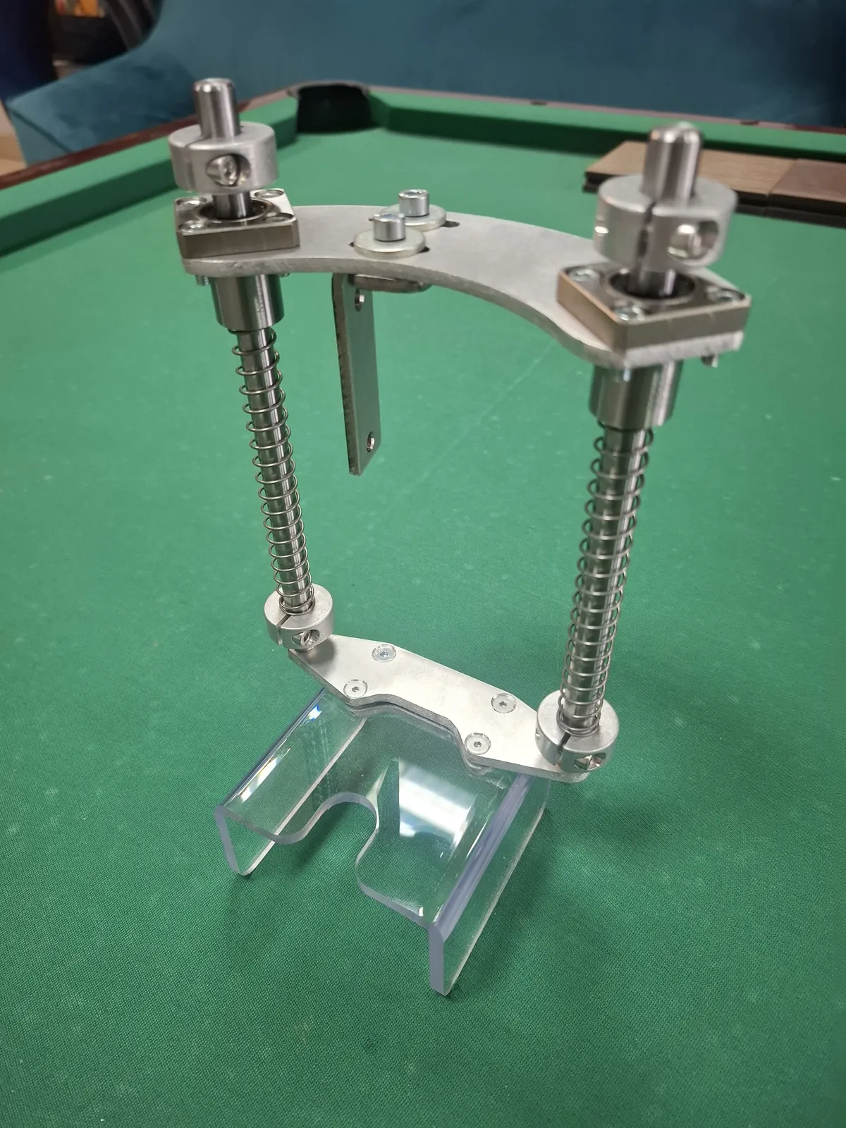 Mechanizm z dwiema śrubami z nakrętkami i przezroczystym elementem u dołu, inne ujęcie